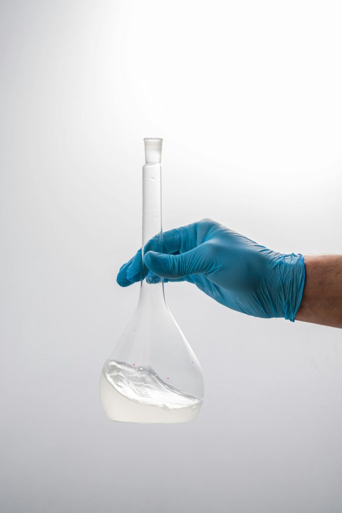 Close-up of a gloved hand holding a volumetric flask in a scientific laboratory setting.